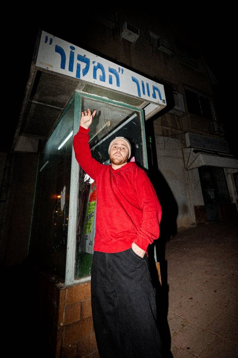 Shahar Solomons on a street corner at night, in a red hoodie